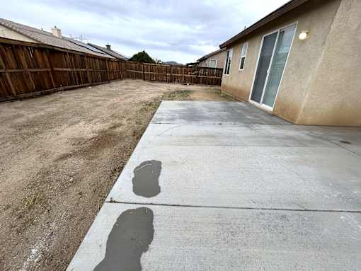 A backyard with a concrete patio and a wooden fence.