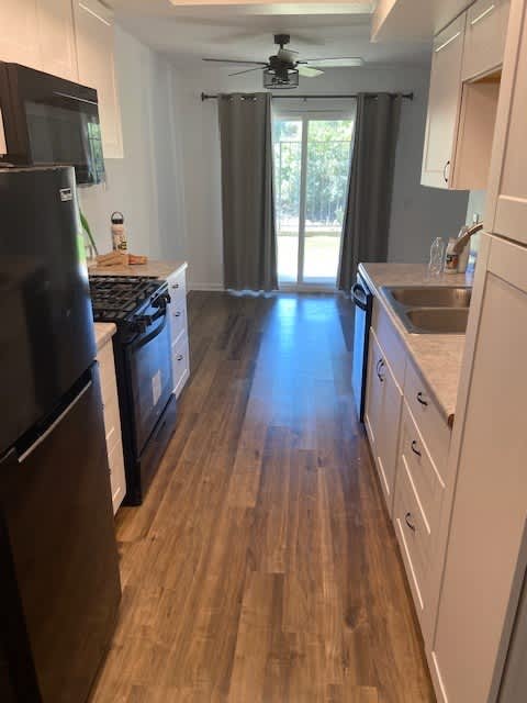 A kitchen with a black fridge and wooden floors.
