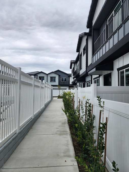 A white fence runs down the side of a sidewalk.
