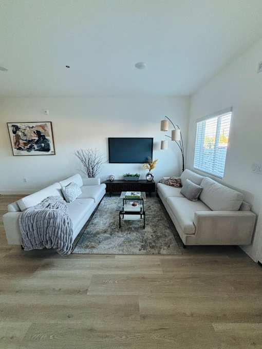 A living room with a white couch, a coffee table, and a flat screen TV mounted on the wall.