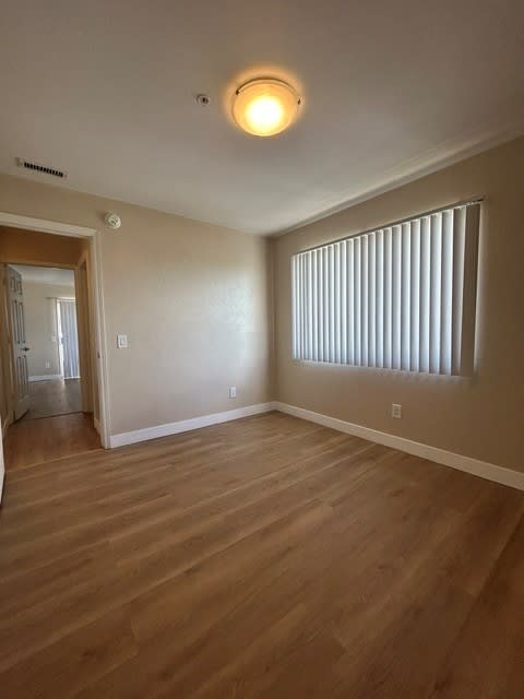 A room with wooden flooring and a window with blinds.