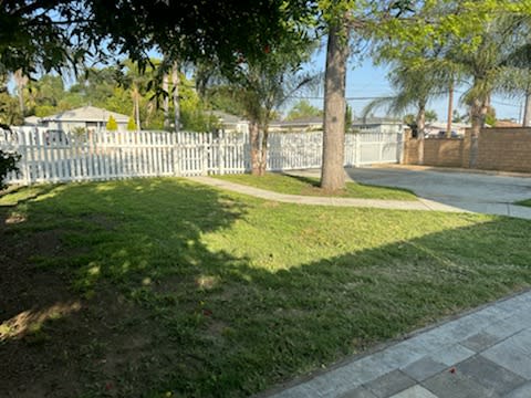 a yard with a white fence and a sidewalk