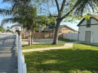 a white house with a fence and a yard with grass and trees