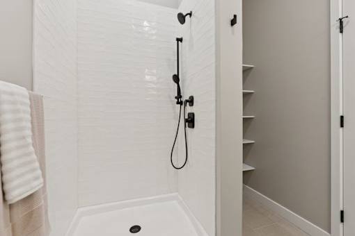 A white tiled shower with a black shower head and hand held shower.