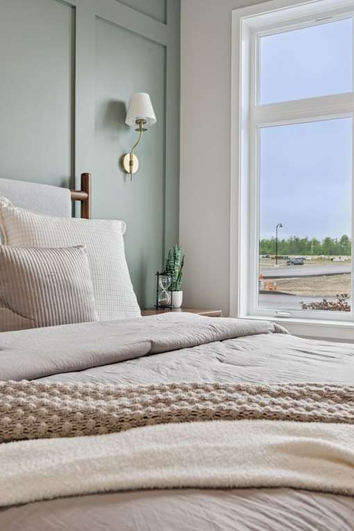 A bedroom with a bed, pillows, a lamp, and a window overlooking a parking lot.