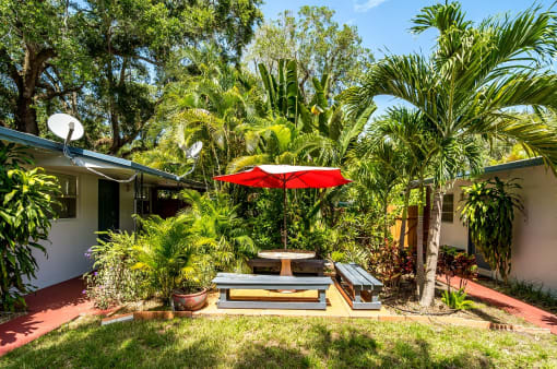 a backyard with a picnic table and a red umbrella