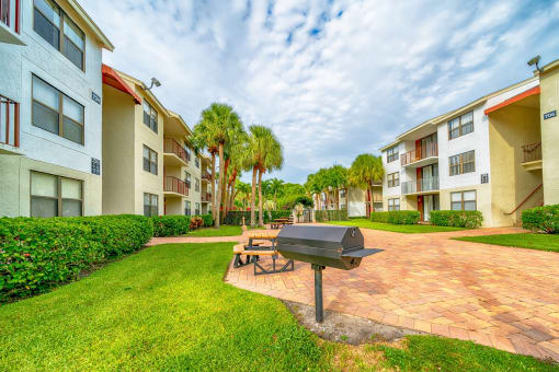 a patio with a grill and picnic table in front of apartment buildings at Bella Lago Vista, West Palm Beach, FL