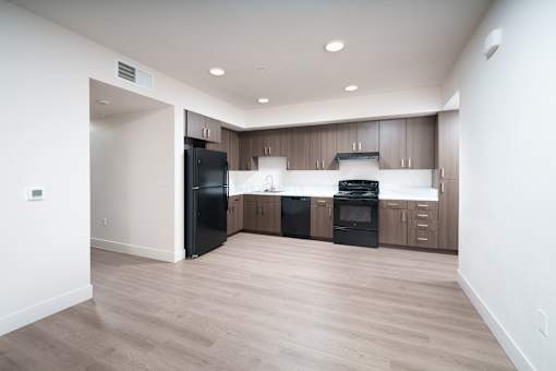 an empty kitchen with wood flooring and a black refrigerator