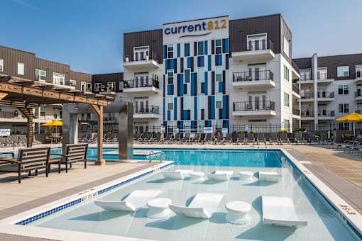 A pool with white chairs and a building with a sign that says "current 812" in the background.