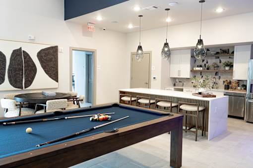 A pool table is in the middle of a room with a bar and kitchen in the background.