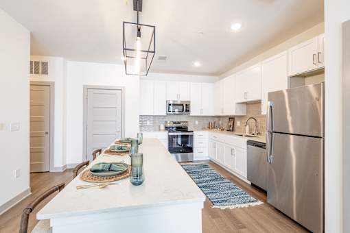 A modern kitchen with a long white island and stainless steel appliances.