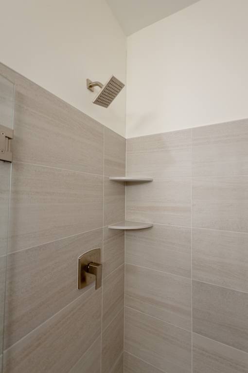 A shower area with a wall-mounted shower head and two shelves.