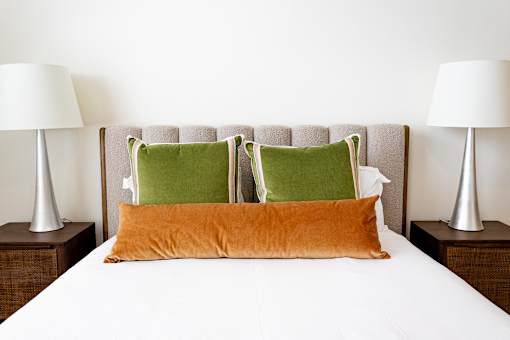 A bed with a white sheet and three pillows, two green and one orange.