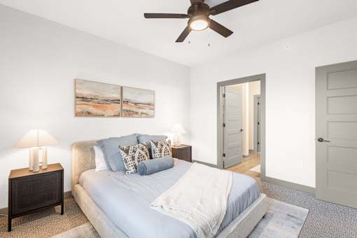 A bedroom with a bed, a ceiling fan, and a painting on the wall.