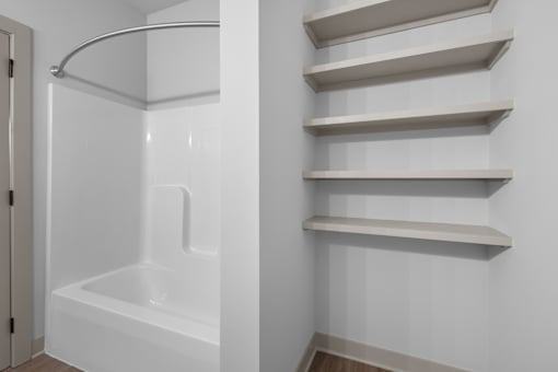 A white bathroom with a tub and shelves.