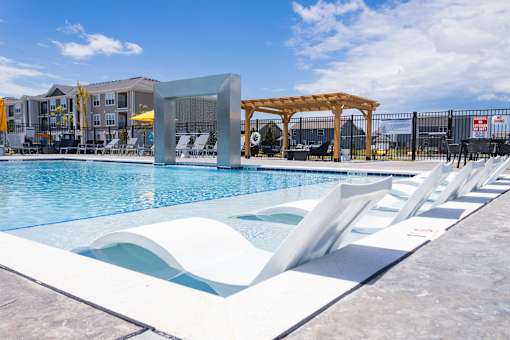Swimming pool with tanning ledge and white loungers at Allure Apartments, Whiteland, IN 46184