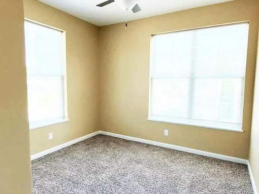 A room with a carpeted floor and two windows.