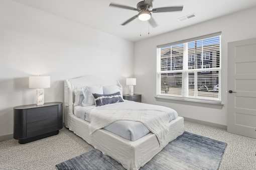 A bedroom with a large bed, a ceiling fan, and a window with blinds at The Warren Apartments, Jeffersonville, IN