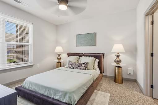 A bedroom with a bed, two lamps, and a painting on the wall at The Warren Apartments, Jeffersonville, IN