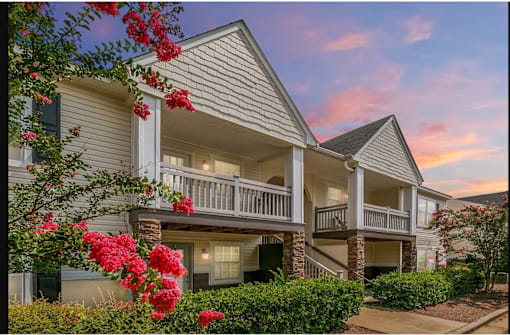 A building with a balcony and a tree with red flowers in front.