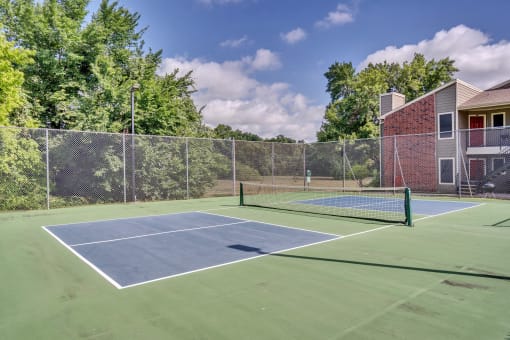 two tennis courts with a house and trees in the background