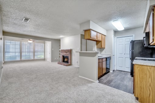 an empty living room with a kitchen and a fireplace