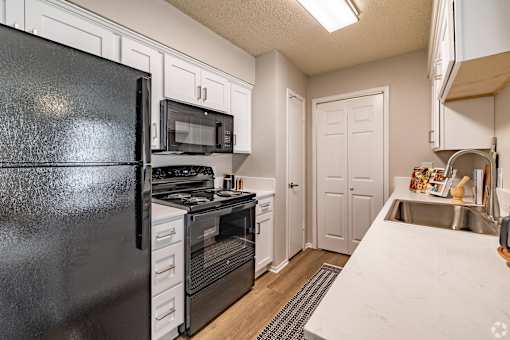 Galley kitchen with white cabinets and black appliances at Highland Park Apartments, Fort Worth