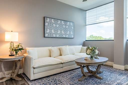 A living room with a white couch, a round table with a vase of flowers, and a framed picture on the wall.
