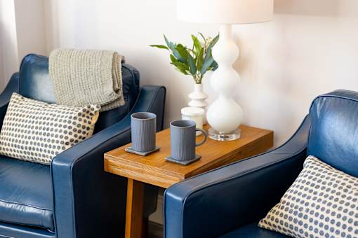 Two grey vases on a table between two chairs.