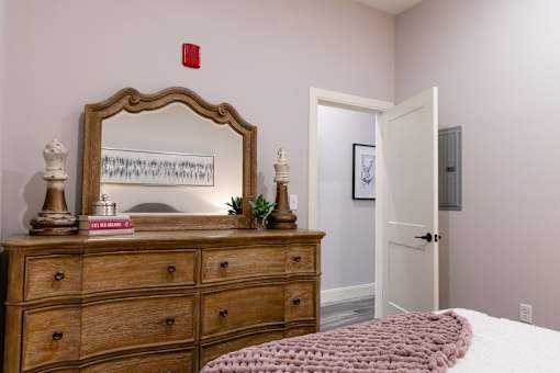 A bedroom with a wooden dresser and a mirror above it.