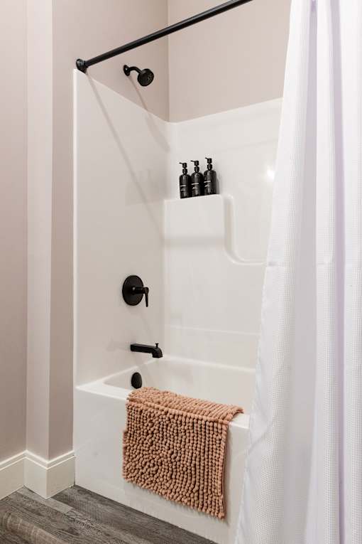 A white bathtub with a brown towel and a white shower curtain.