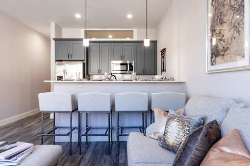 A modern kitchen with a bar stool and a grey couch with pillows.