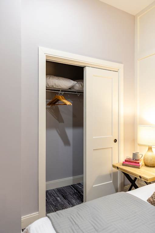 A white door is open to a small closet with a hanger and a pillow.