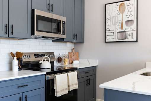A kitchen with a white counter top and a picture of a whiskey glass and a spoon on the wall.