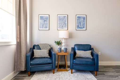 Two blue chairs with pillows and a small table between them.