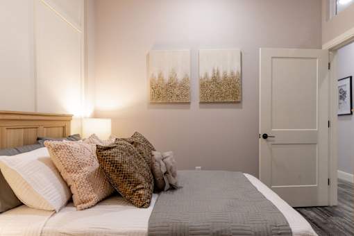 A bedroom with a bed, two pillows, a lamp, and two paintings on the wall.