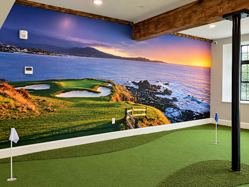 A room with a golf putting green and a large picture of a golf course on the wall.