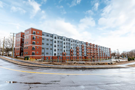 Apartment building with a red brick facade and a parking lot in front.