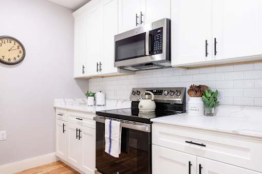 A white kitchen with a black stove top oven and a microwave above it.