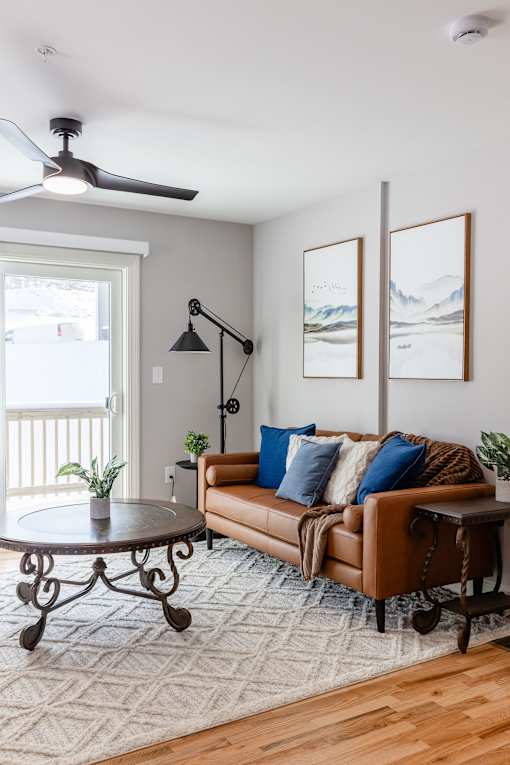 A living room with a brown leather couch, a round table, and two framed pictures on the wall.