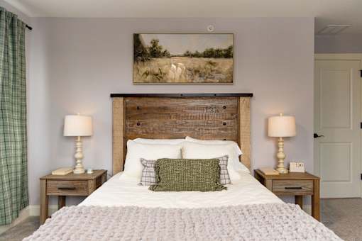 A bedroom with a large bed, two lamps, and a painting on the wall.