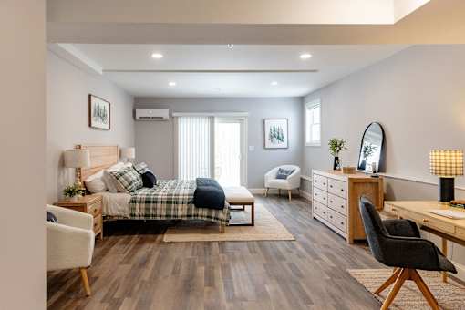 A well-lit bedroom with a bed, chair, and desk.