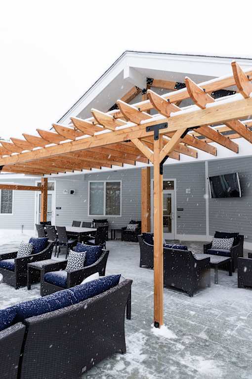 A wooden pergola over a patio with black wicker furniture.