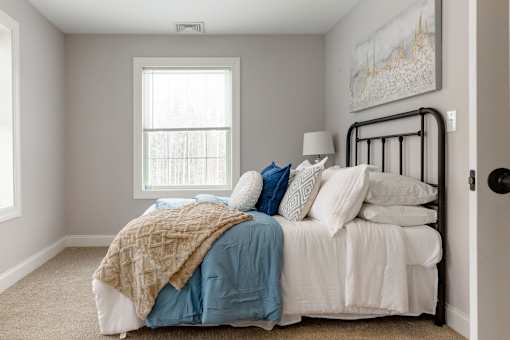 A bed with a white comforter and a blue blanket is in a room with a window.