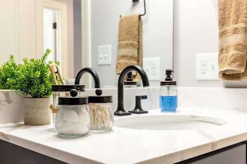 A bathroom sink with a black faucet and a jar of cotton balls on the counter.