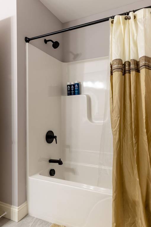 A shower with a yellow curtain and a black handle.