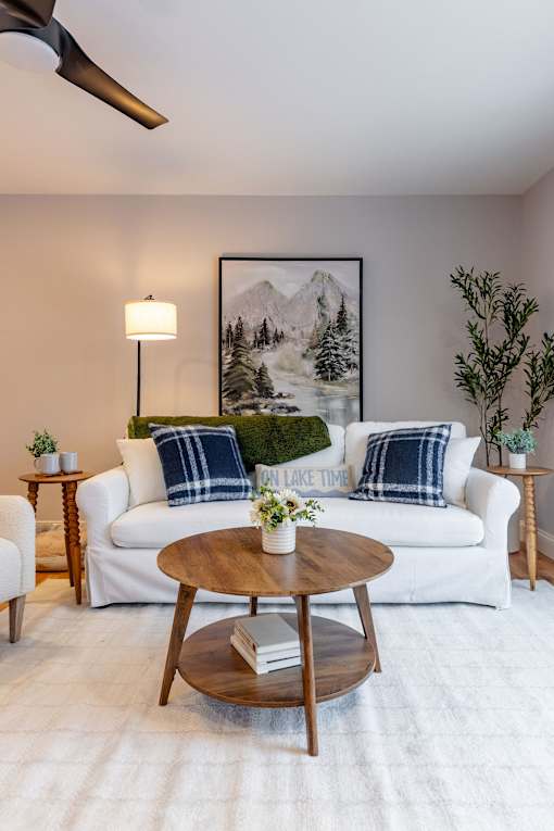 A living room with a white couch, a wooden coffee table, and a painting of a mountain landscape on the wall.