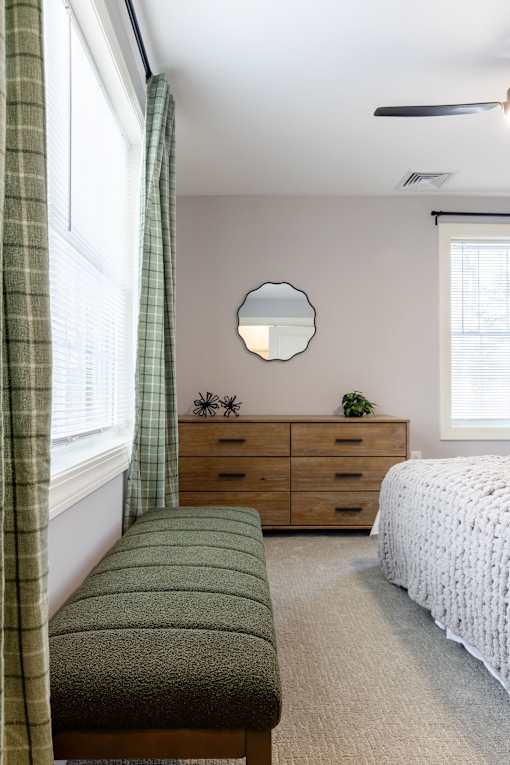 A bedroom with a bed, a dresser, and a window with curtains.