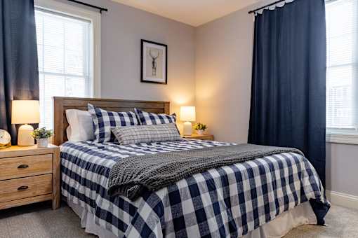 A bed with a checkered comforter and pillows is in a room with a window and a nightstand.