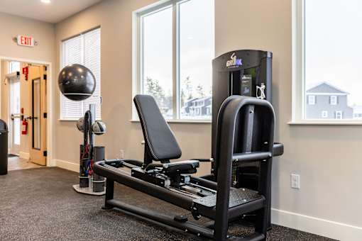A gym room with a rowing machine and a ball on the floor.